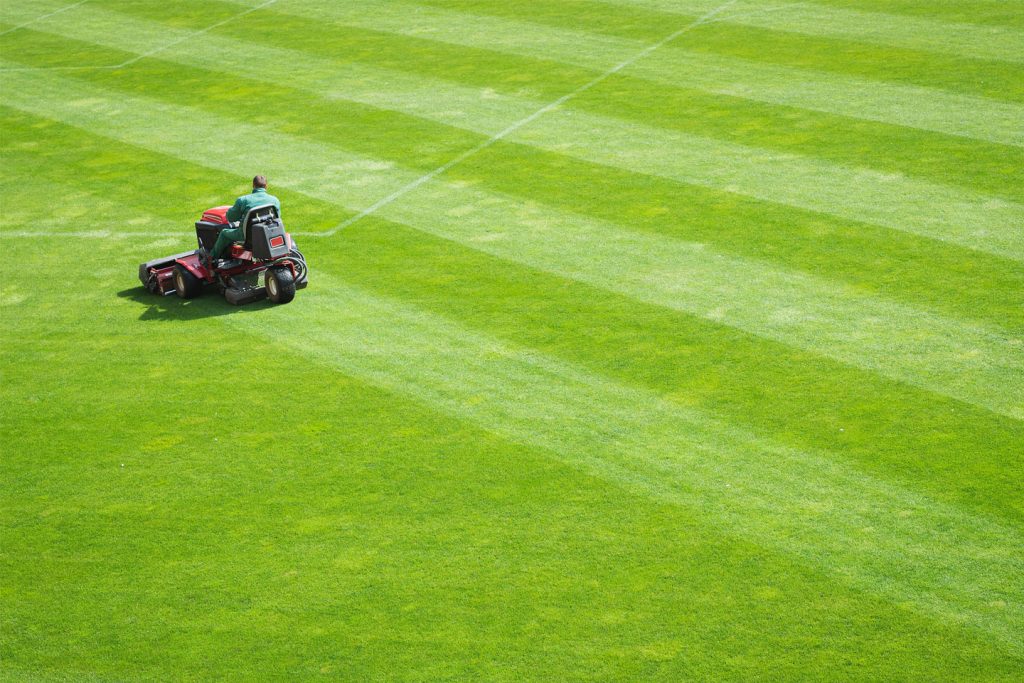 Man on lawnmower mowing a baseball outfield