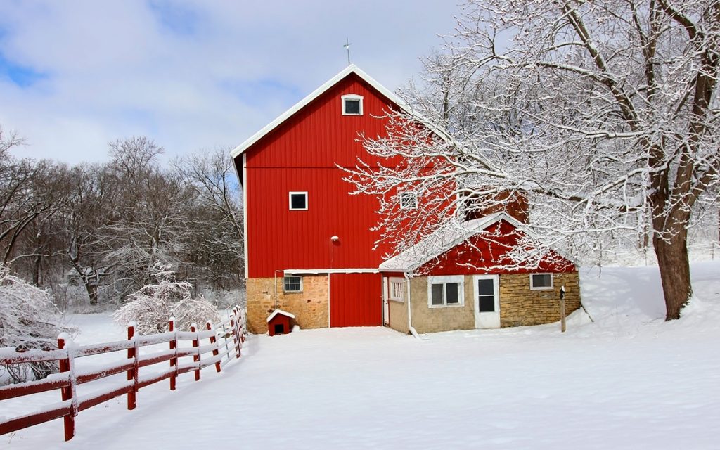 Red barn on a very snowy day with snow covered trees and yard